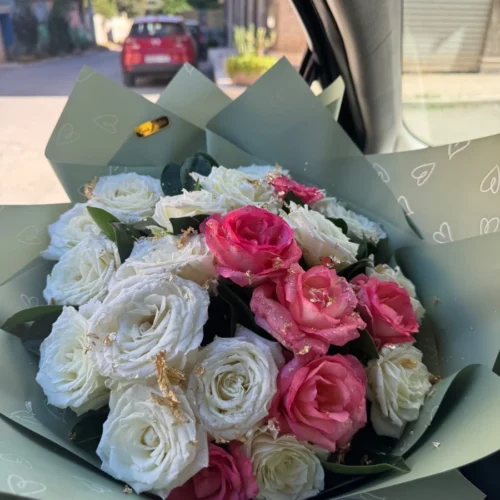Bouquet de roses blanches et roses fraîches dans un papier vert pastel, présenté en voiture