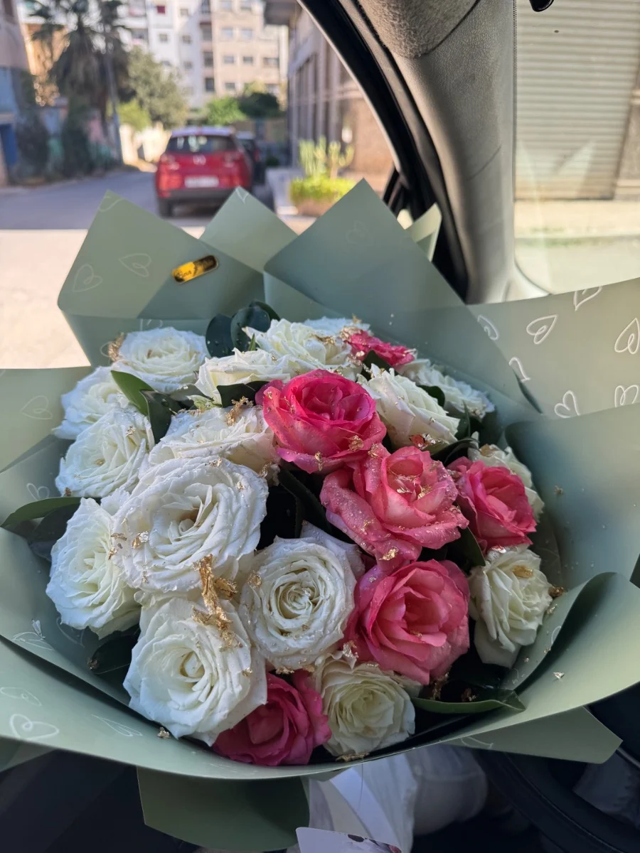 Bouquet de roses blanches et roses fraîches dans un papier vert pastel, présenté en voiture