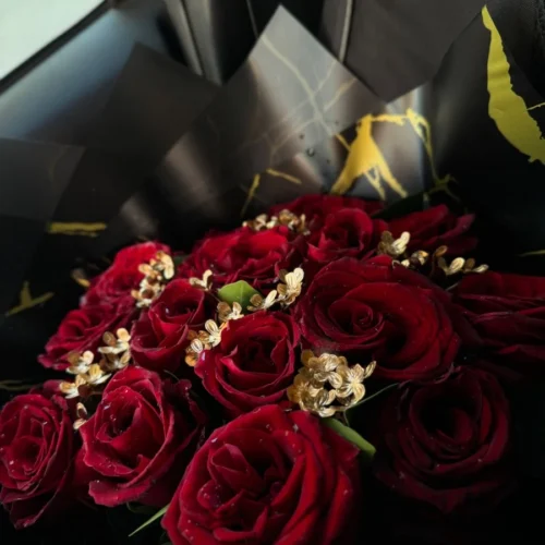 Bouquet de roses rouges avec décorations dorées dans un emballage noir élégant