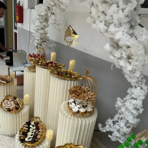 Buffet de luxe à Fès avec présentoirs blancs, plateaux dorés, douceurs et arche florale blanche